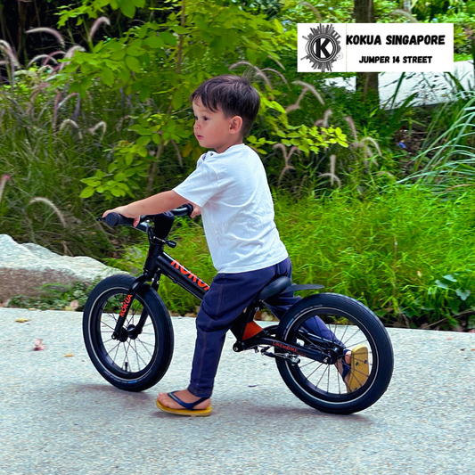 a young boy riding a KOKUA Jumper 14 black bike down a street