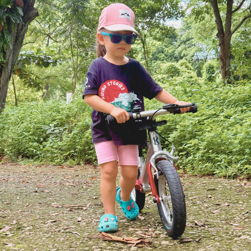 A young girl riding her KOKUA Jumper 12 Street Edition balance bike in red