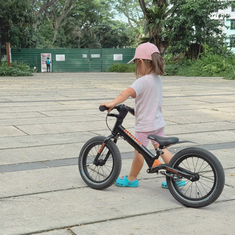 A young boy riding his KOKUA Jumper 14 Street Edition balance bike in black