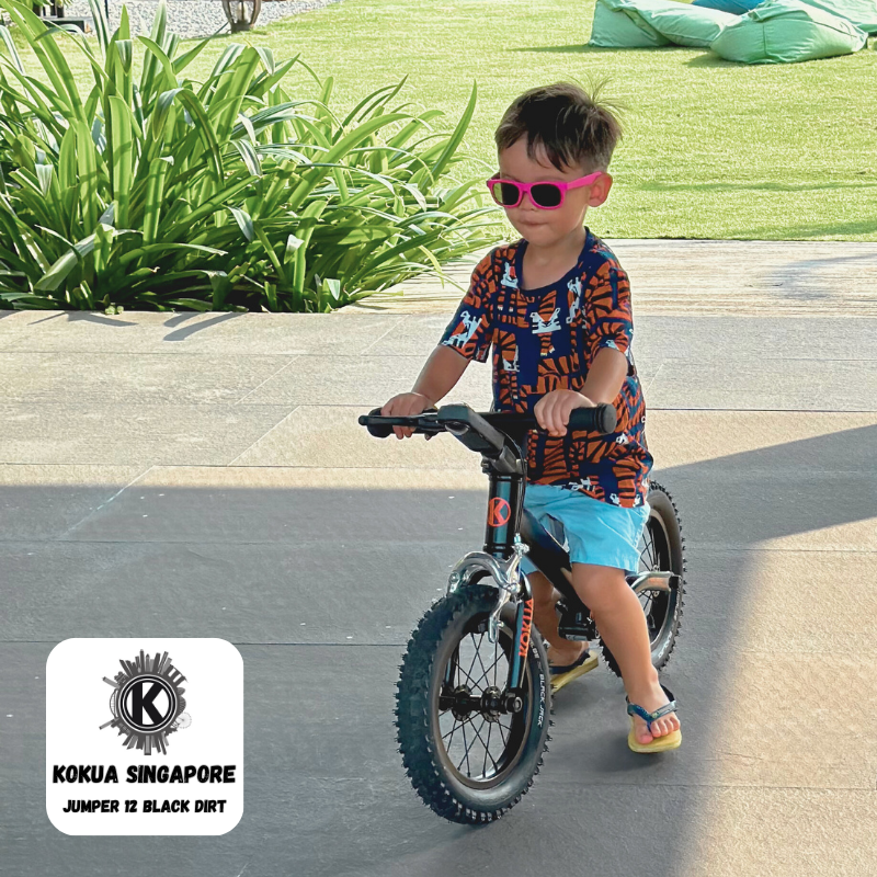 a young boy riding a KOKUA Jumper 12 Balance bike on a sidewalk