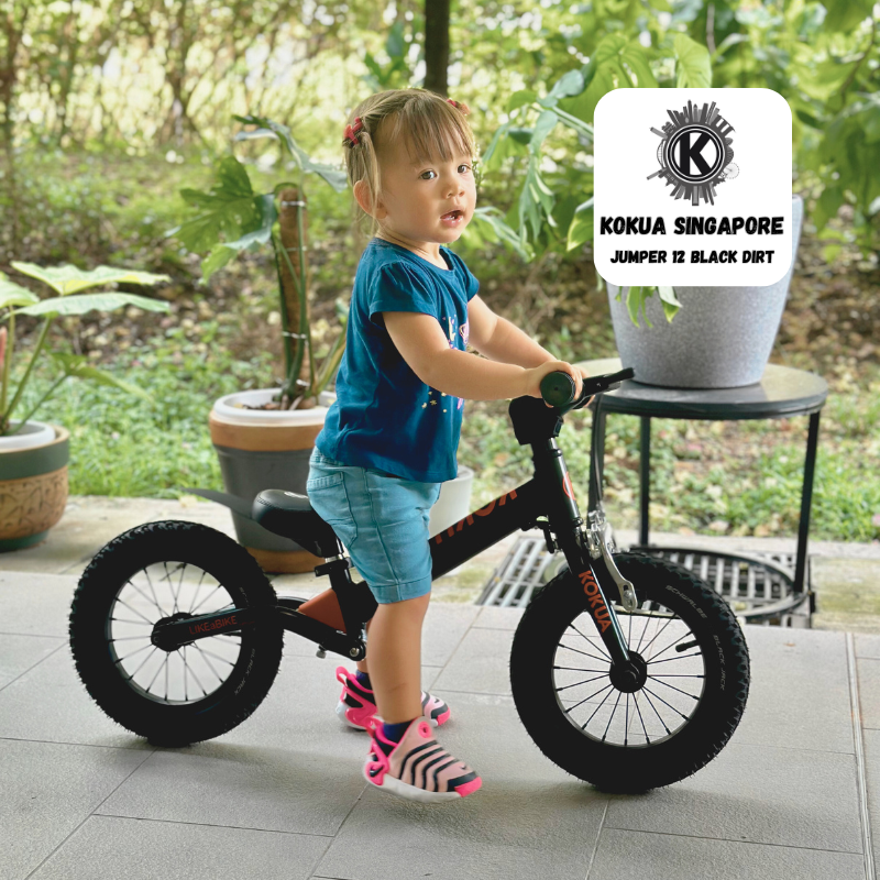 a little girl riding a small KOKUA Jumper 12 balance black bike