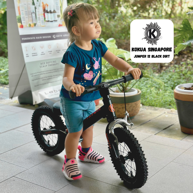 a little girl riding a KOKUA Jumper 12 balance bike on a sidewalk