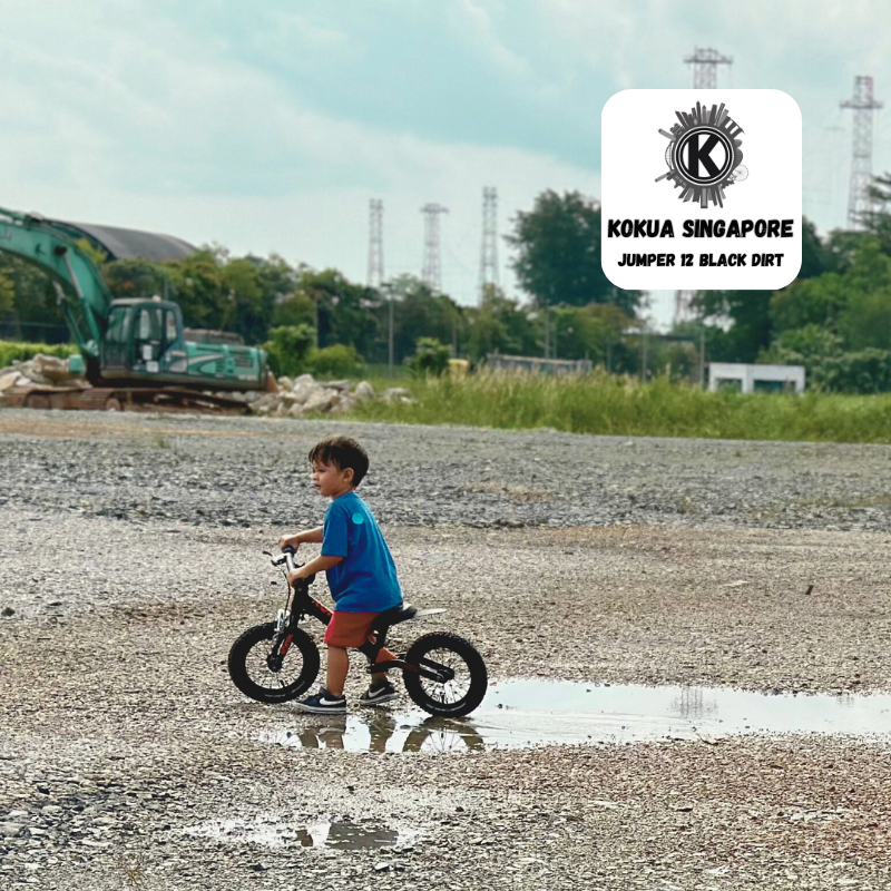 a young boy riding a KOKUA Jumper 12 balance bike through a puddle of water