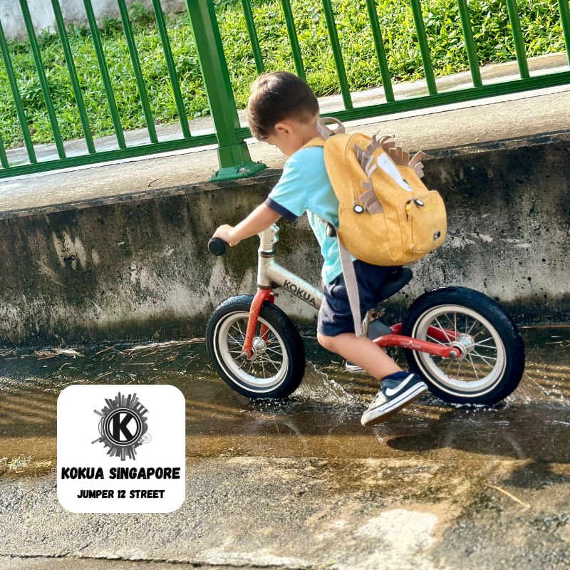 a young boy riding a KOKUA Jumper 12 balance bike through a puddle of water