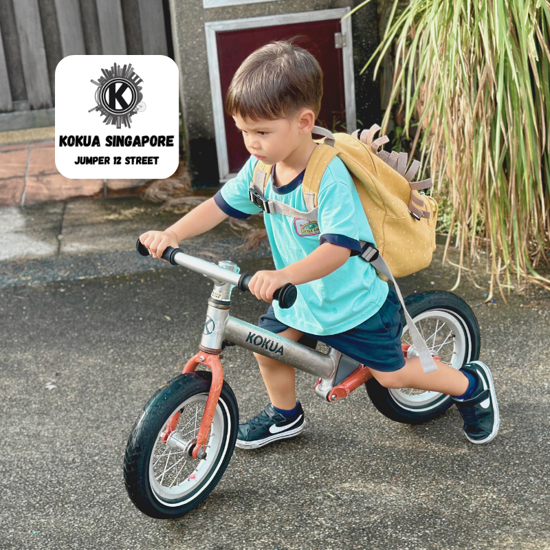 a young boy riding a KOKUA Jumper 12 balance bike with a back pack