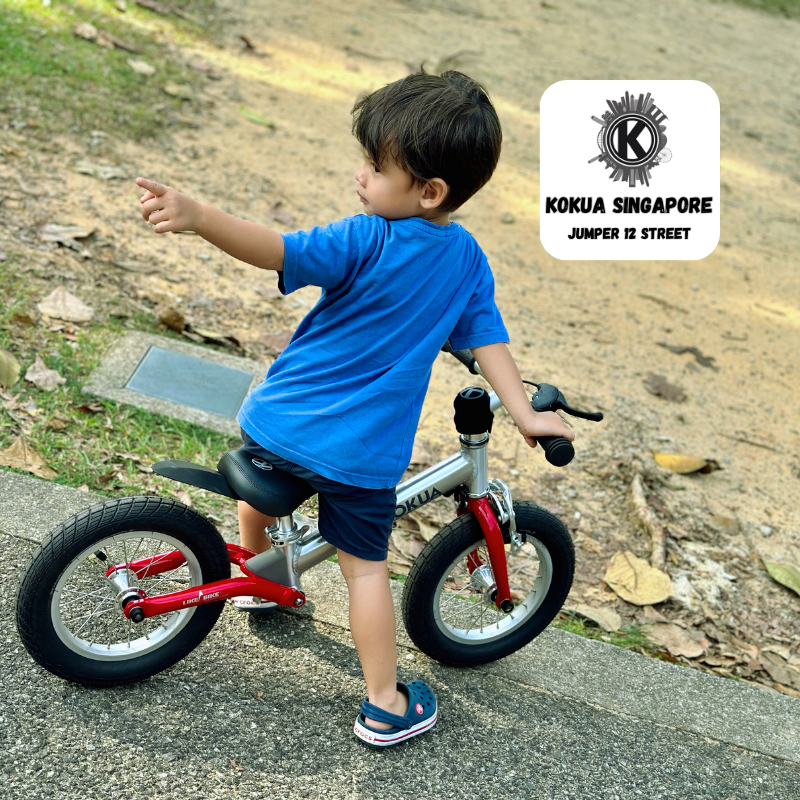 a young boy riding a red and blackKOKUA Jumper 12 balance bike