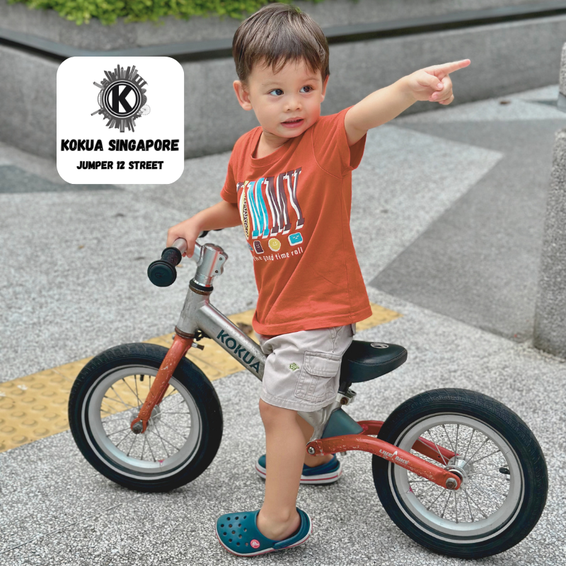 a young boy riding a KOKUA Jumper 12 balance bike on a sidewalk