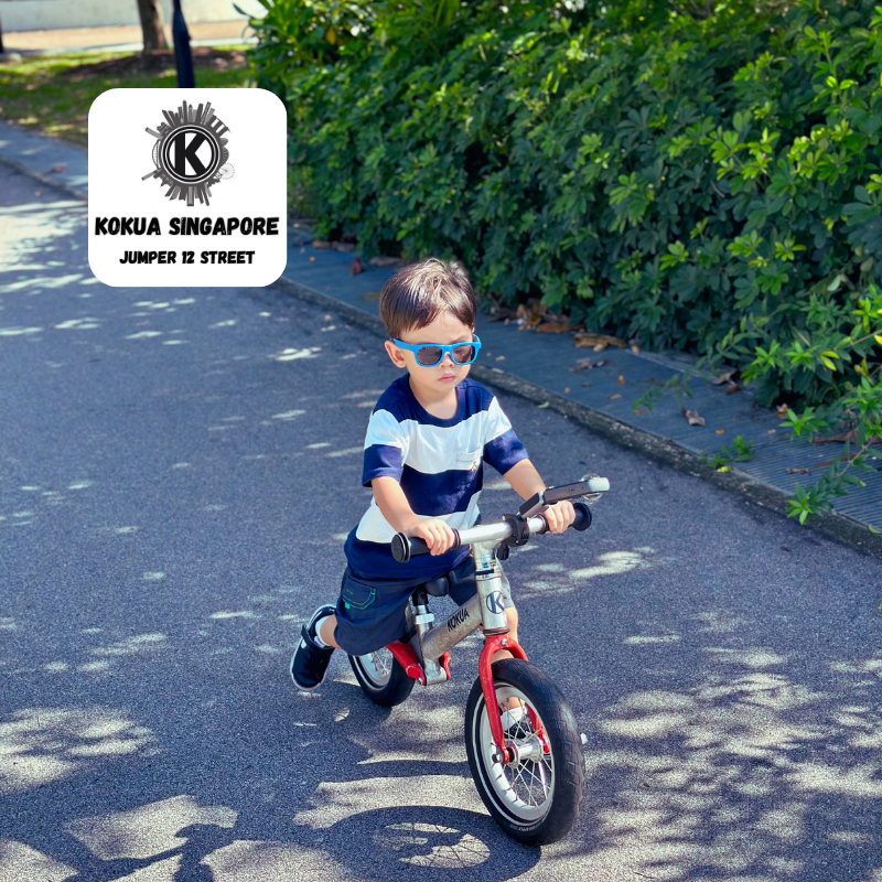 a young boy riding a redKOKUA Jumper 12 balance bike down a street