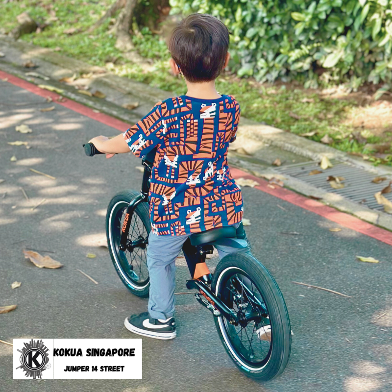 a young boy riding a KOKUA Jumper 14 balance bike down a street