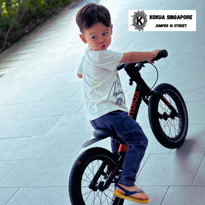 a young boy riding a KOKUA Jumper 14 balance bike on a sidewalk