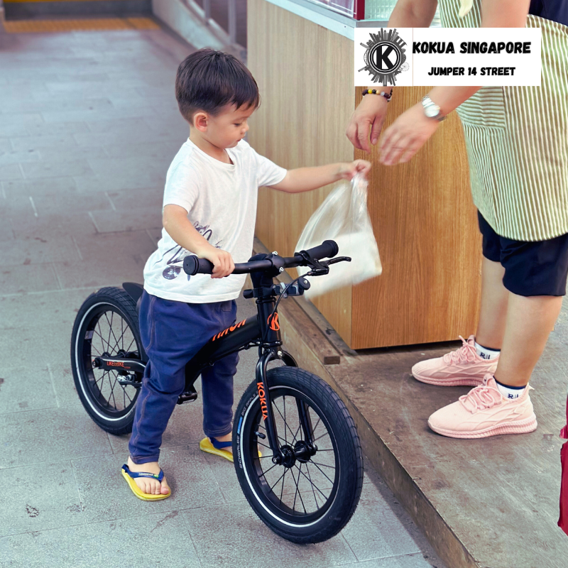 a young boy on a KOKUA Jumper 14 balance bike is handing a bag to a woman