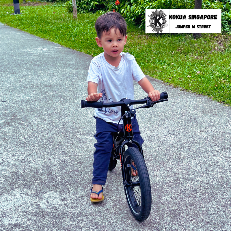 a young boy riding a KOKUA Jumper 14 balance bike down a sidewalk