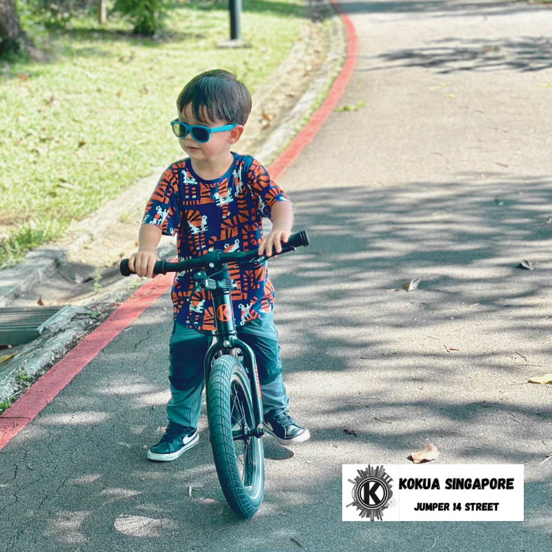 a young boy riding a KOKUA Jumper 14 balance bike down a street