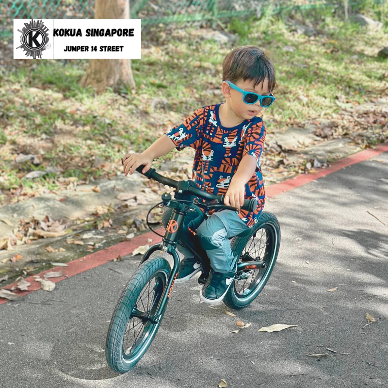 a young boy riding a KOKUA Jumper 14 balance bike down a street