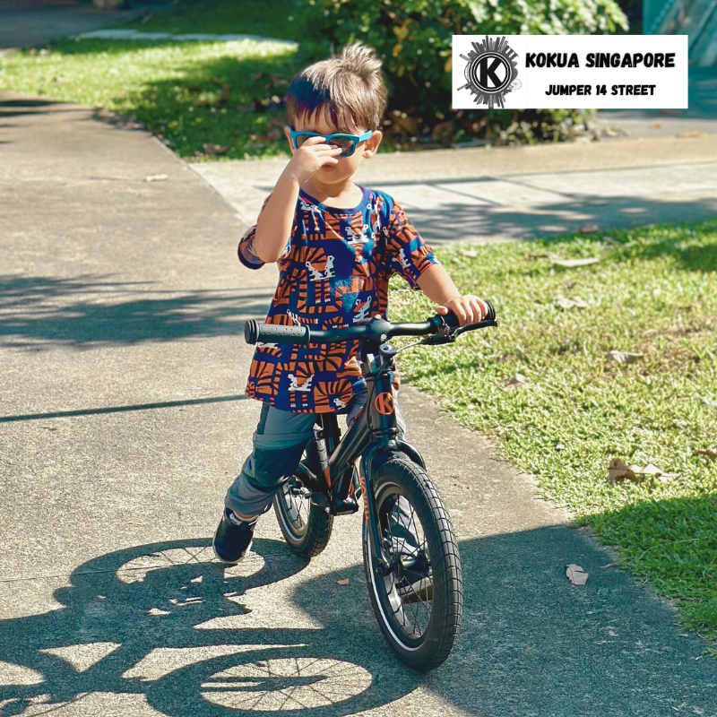 a young boy riding a KOKUA Jumper 14 balance bike down a sidewalk