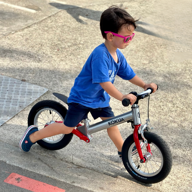 a young boy riding a KOKUA Jumper 12 balance bike down a street